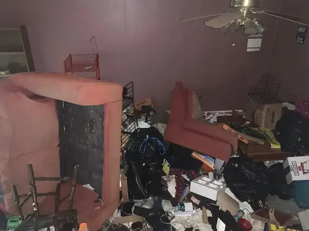 The inherited house as he found it — a living room filled floor to ceiling with furniture, bin bags and boxes, an overturned armchair against a mauve wall.